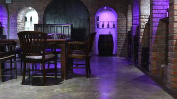 A brick-walled room with wooden chairs and tables, a wine rack, and a barrel.