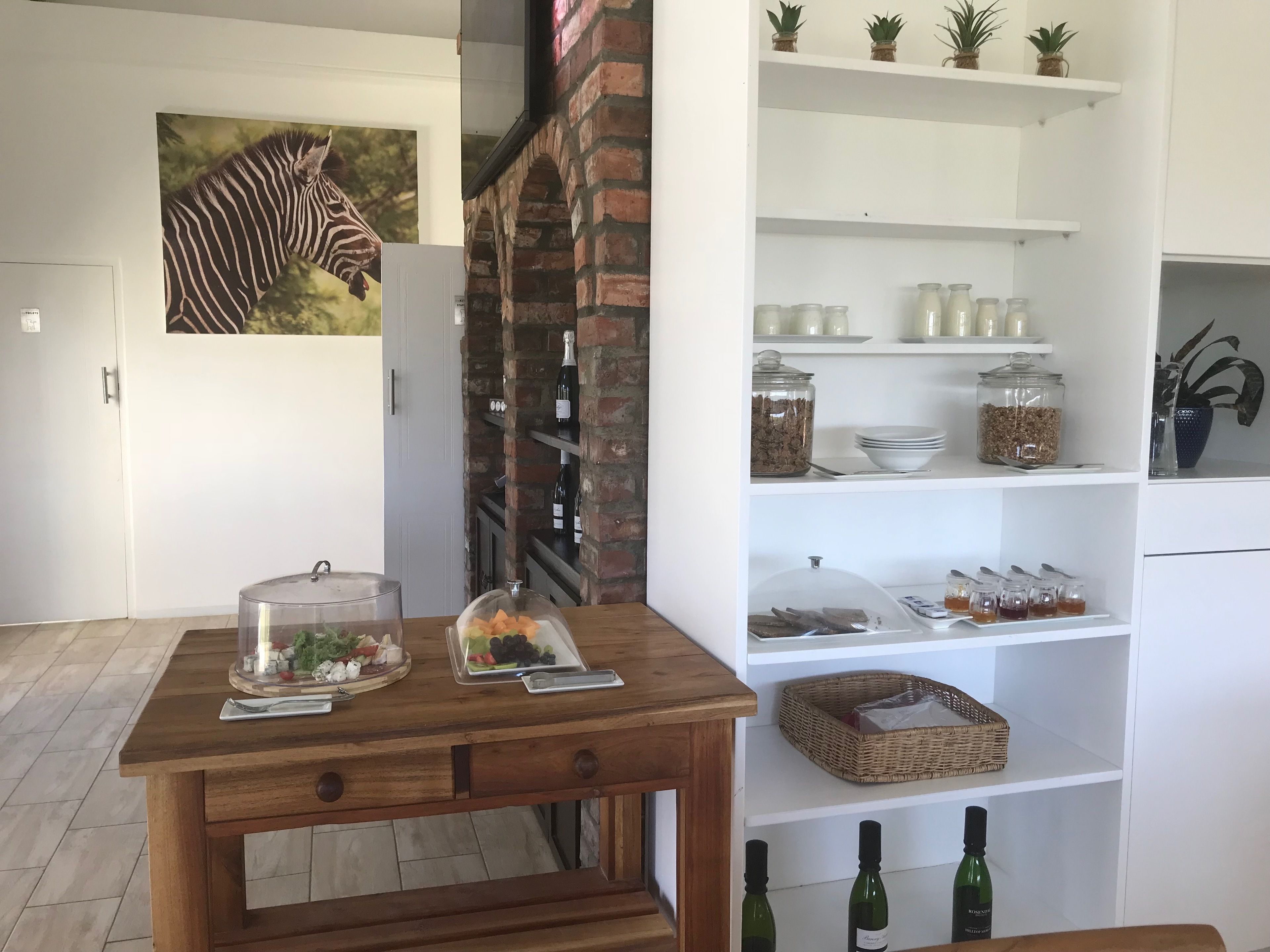 A modern kitchen with a brick wall, a zebra mural, and a wooden table with food and drink items.