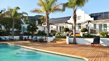 Uma área à beira da piscina com deck de madeira, espreguiçadeiras e piscina.