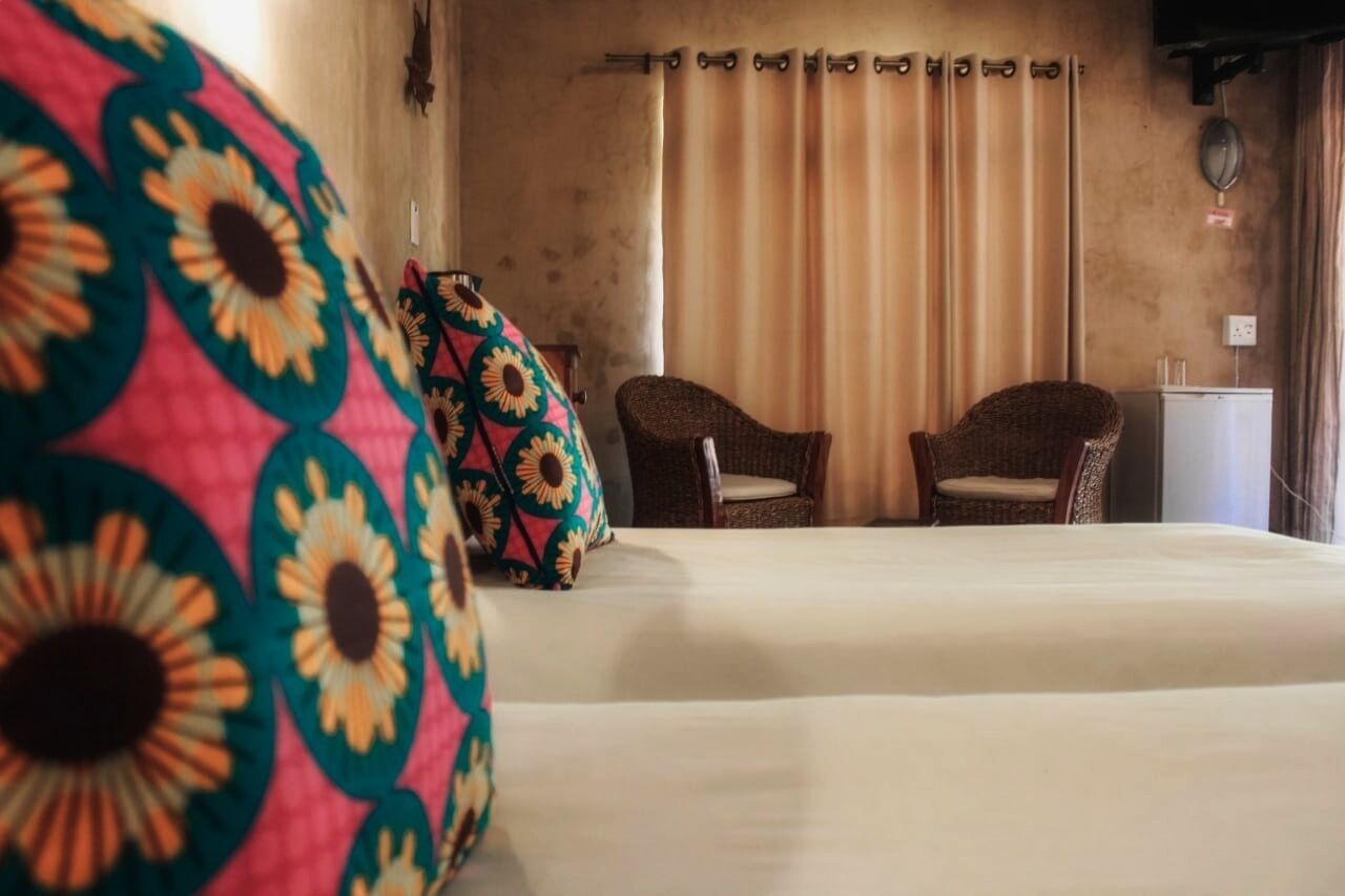 A hotel room with a bed, two wicker chairs, a small table, and a curtain.