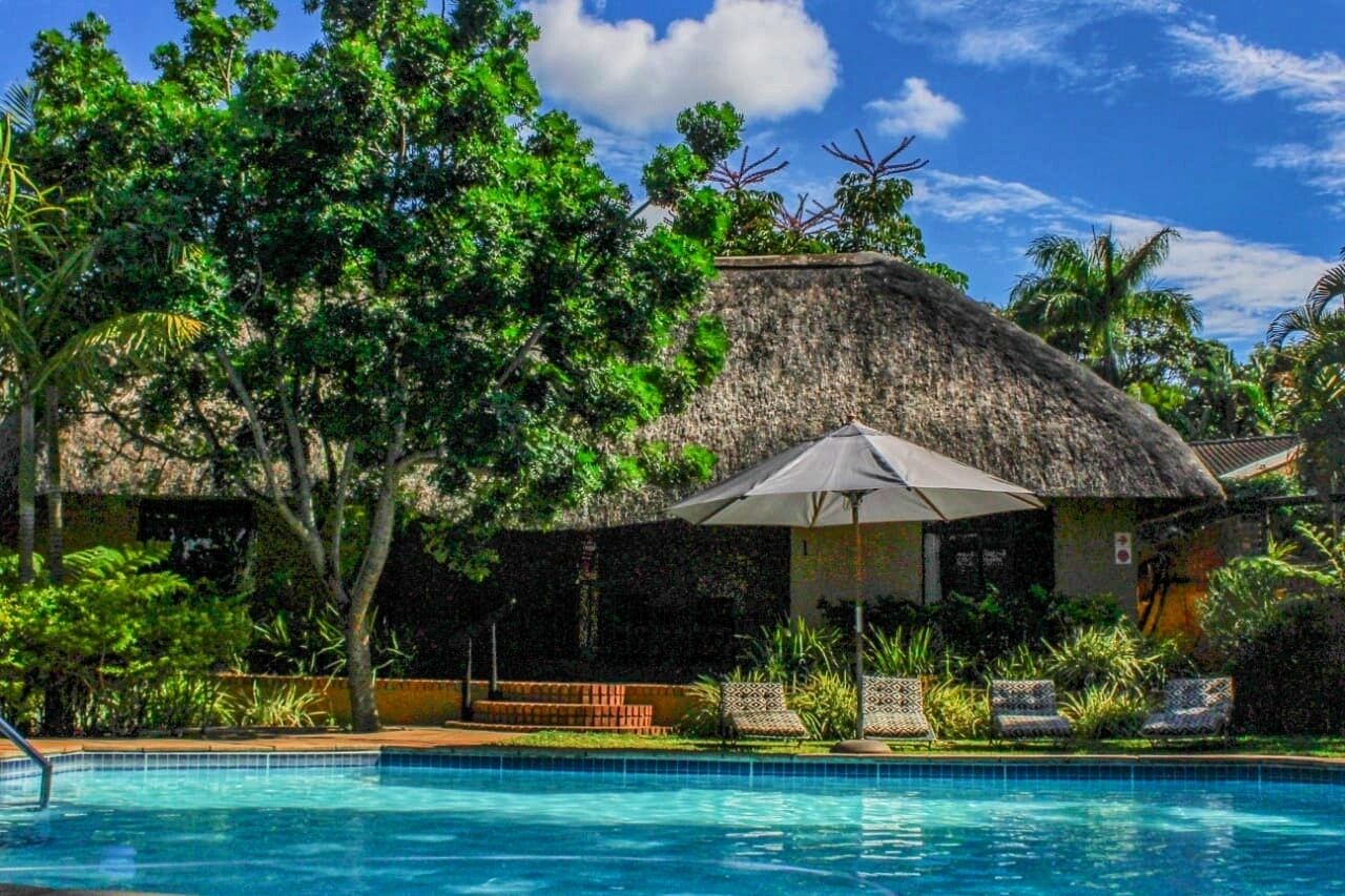 A pool area with a thatched-roof structure, lounge chairs, and lush greenery.