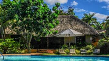A pool area with a thatched-roof structure, lounge chairs, and lush greenery.