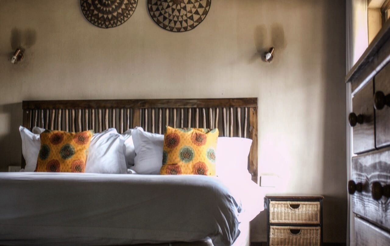 Un lit avec des oreillers blancs et à motifs, une tête de lit en bois et une table de chevet avec un panier.
