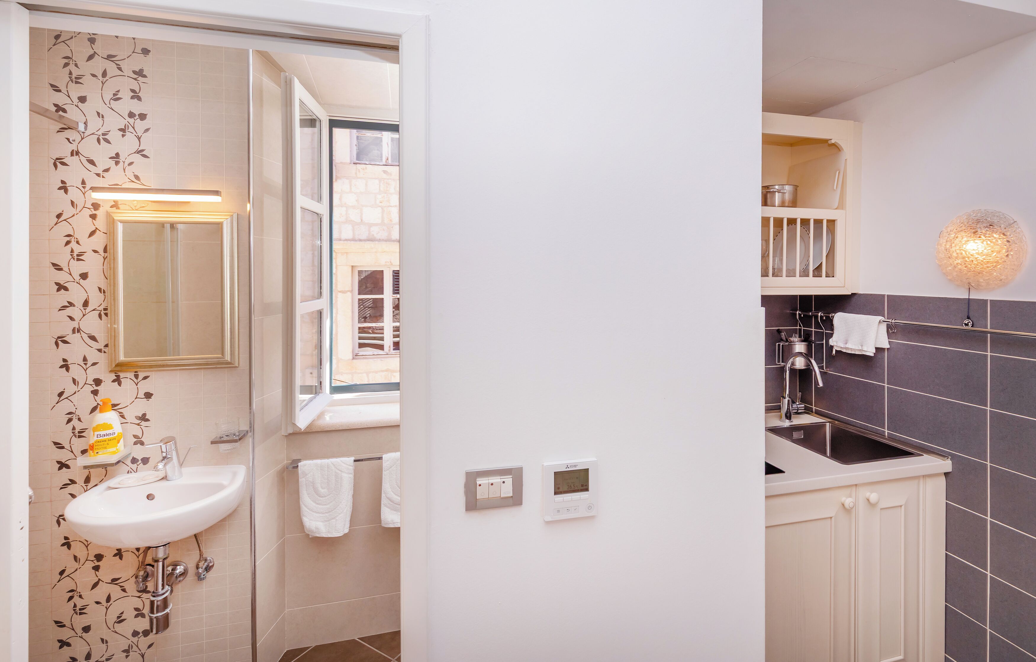 A bathroom with a white sink, a mirror, and a window. There are towels hanging on the wall and a light fixture above the sink.