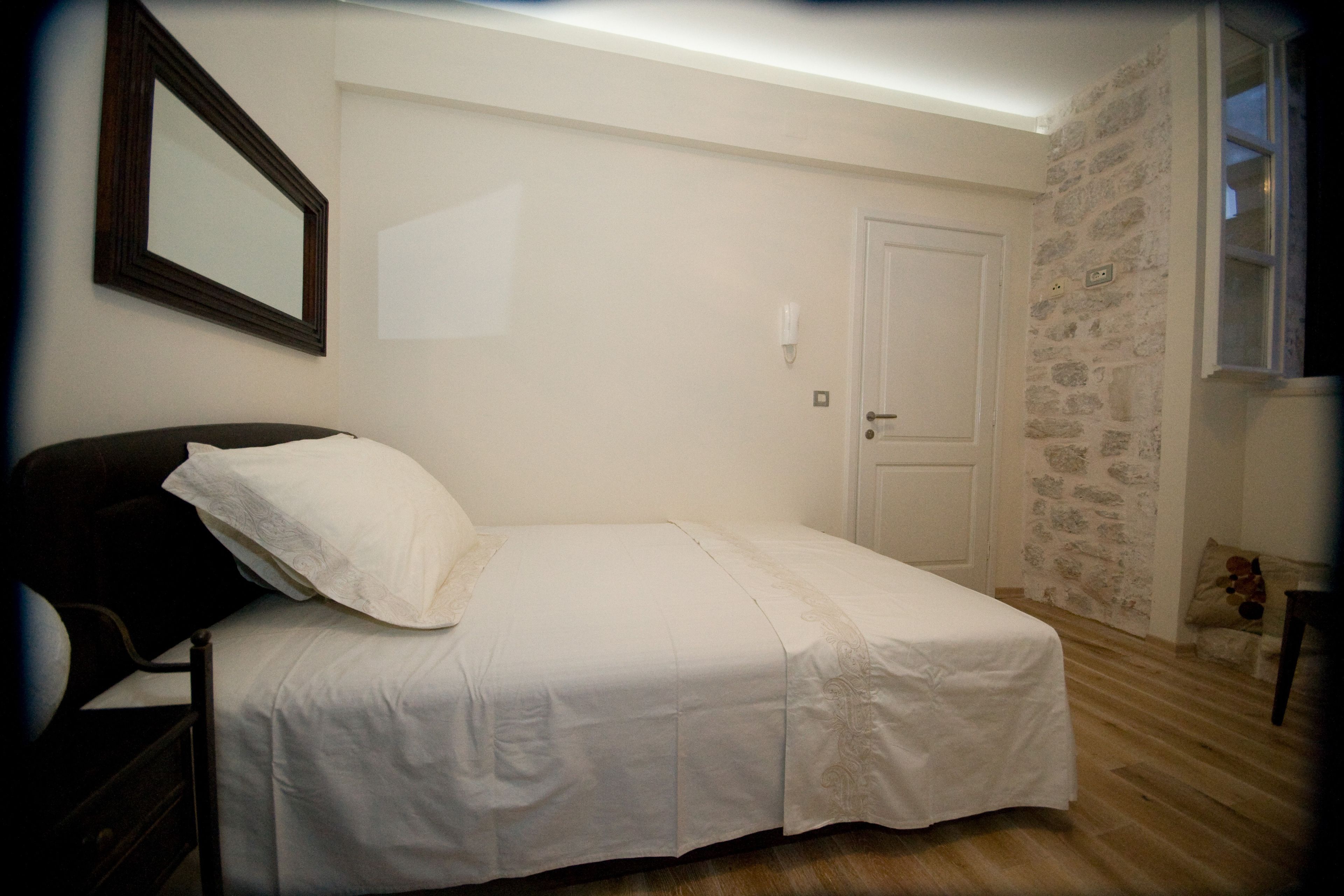 A small, neatly arranged bedroom with a single bed, a door, and a stone wall.
