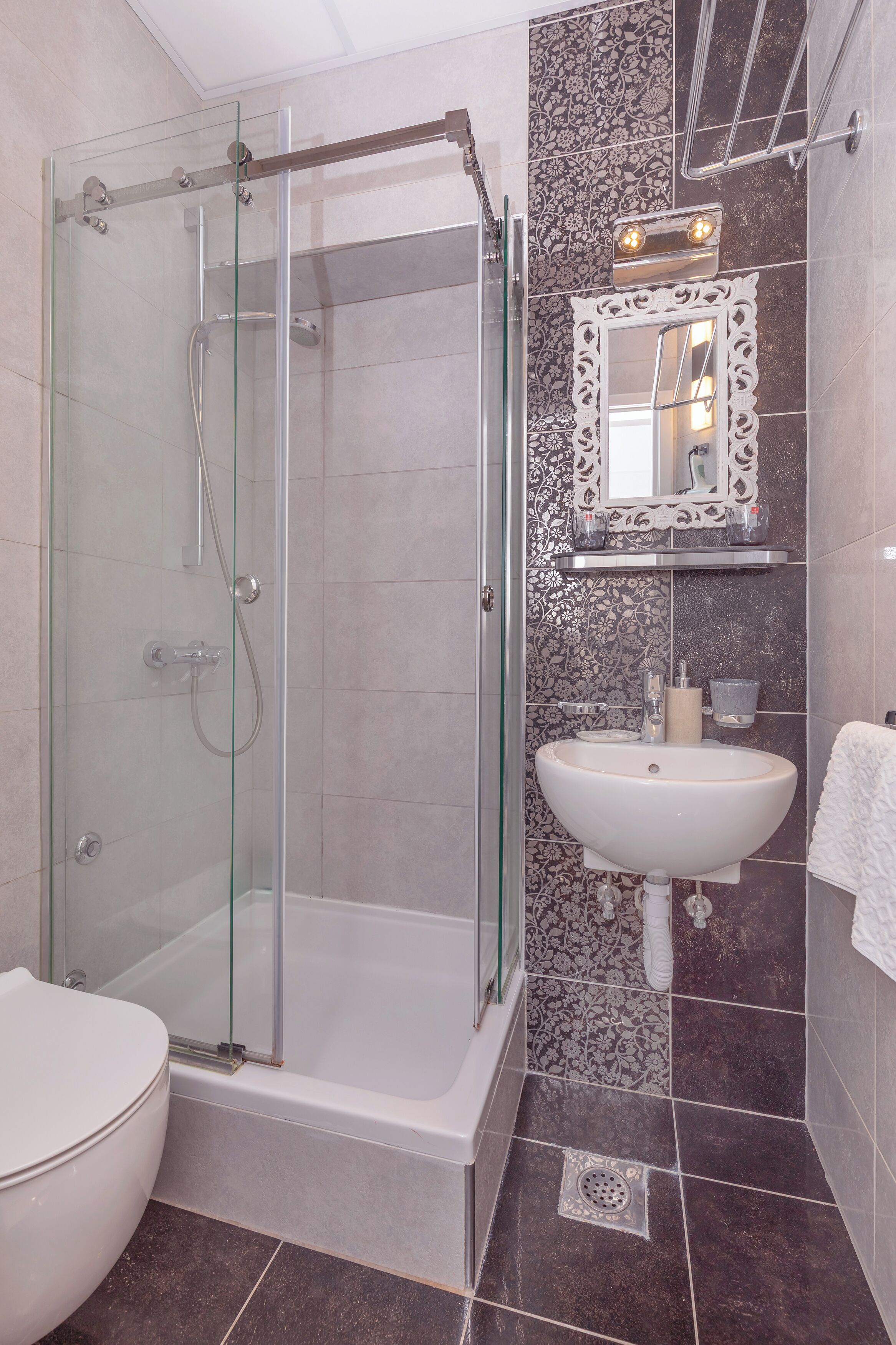 A modern bathroom with a glass-enclosed shower, a white sink, and a decorative mirror.