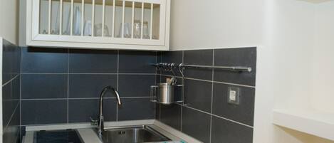 A kitchen with a sink, stove, and a shelf above the sink holding kitchenware.