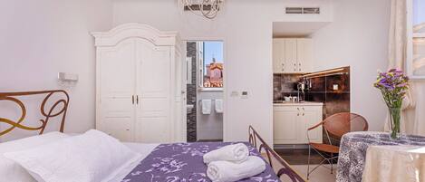 Un dormitorio con cama, una silla, una mesa con un florero y vistas a la cocina.