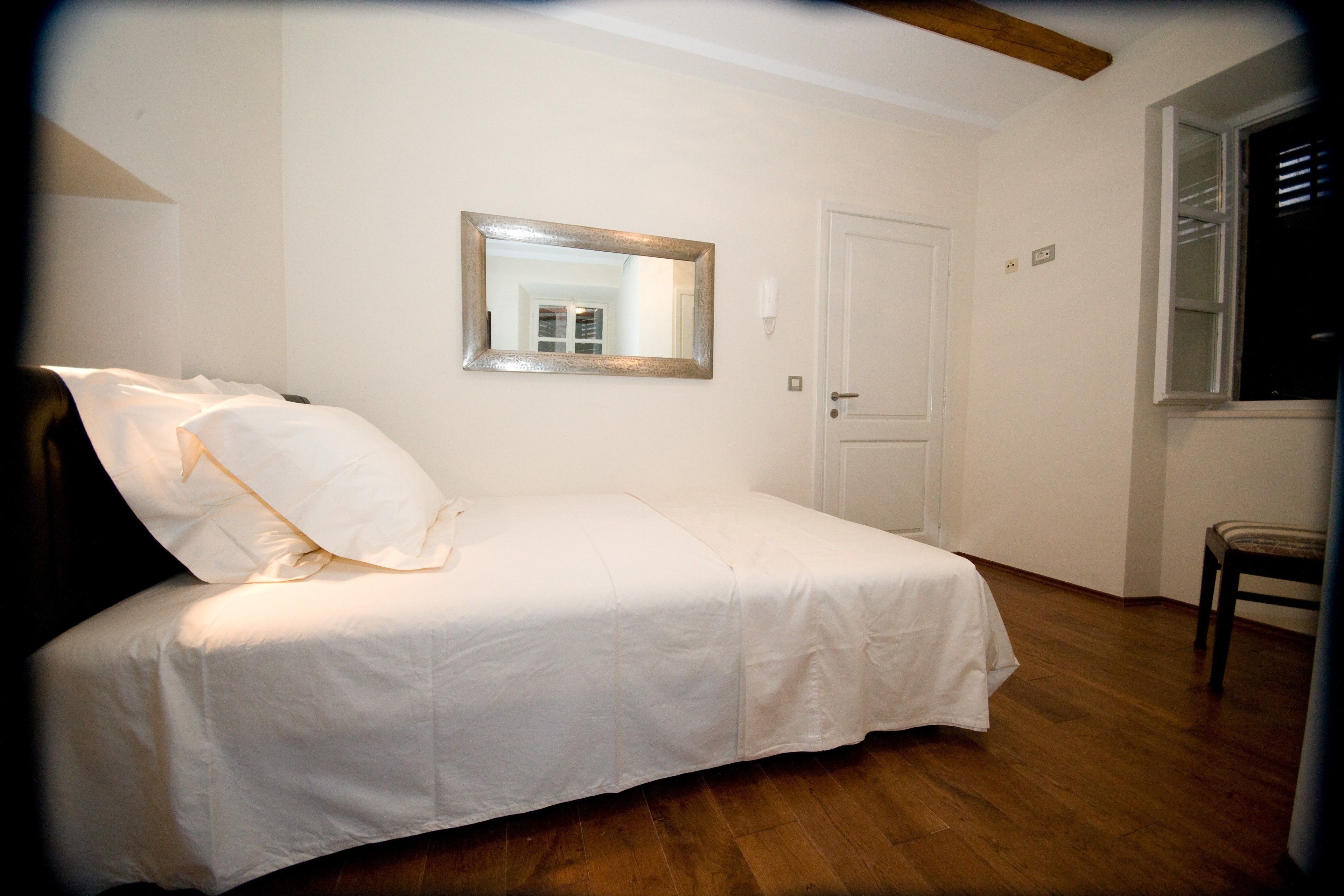 Quarto com uma cama de solteiro, um espelho, uma porta e uma janela.
