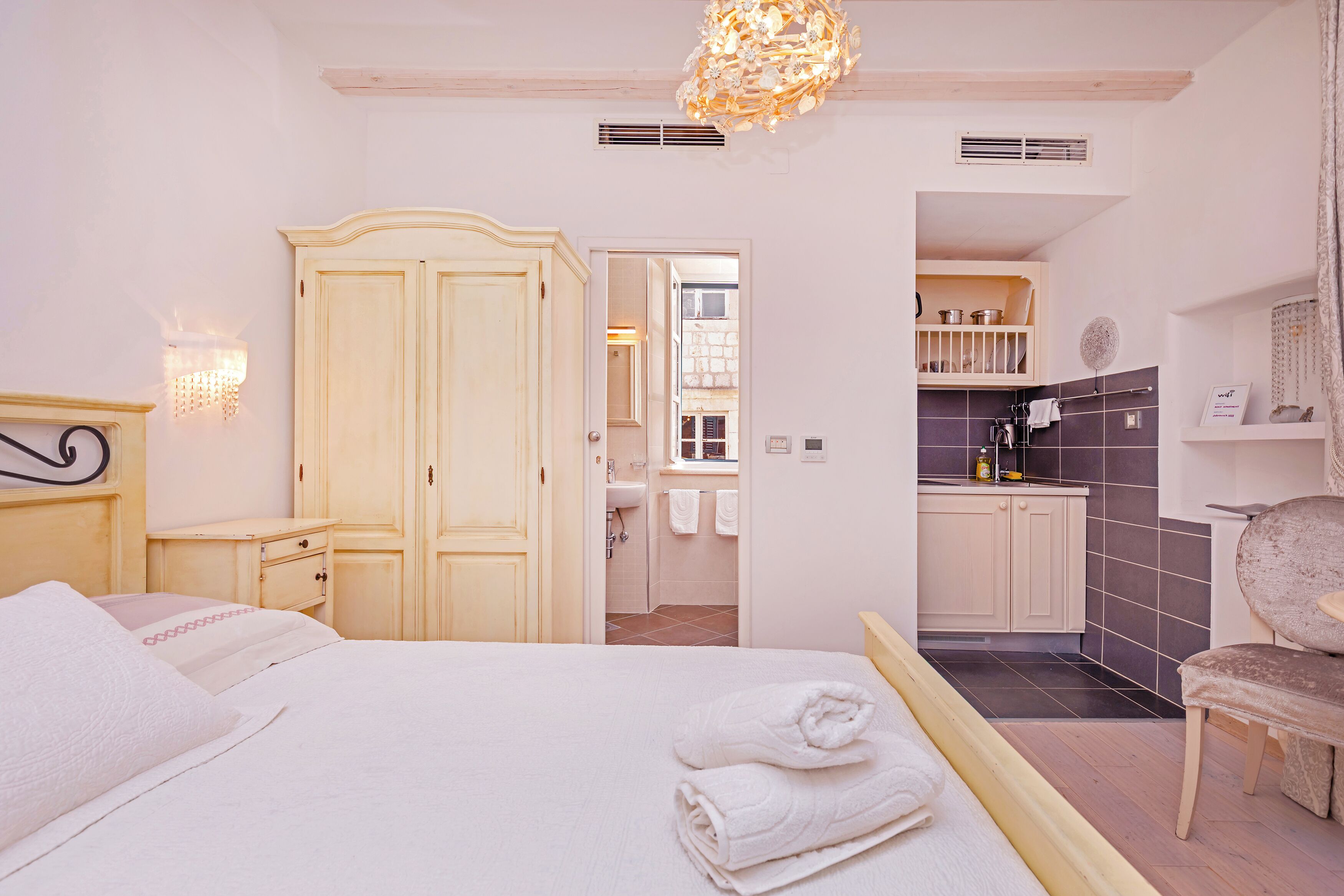 A bedroom with a bed, a wardrobe, a chair, and a bathroom visible through an open door.