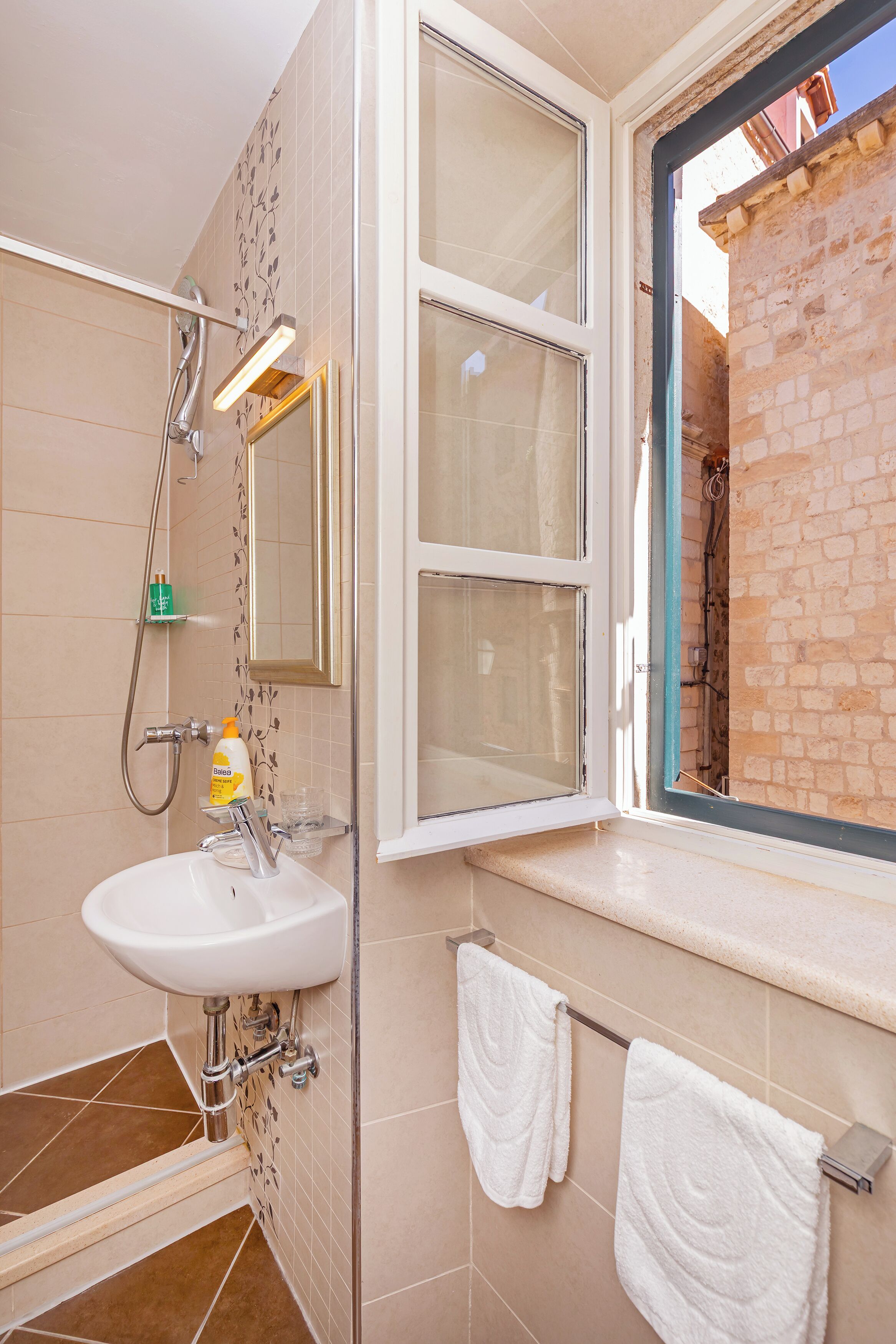 A bathroom with a sink, mirror, towel rack, and a window with a view of a brick wall.