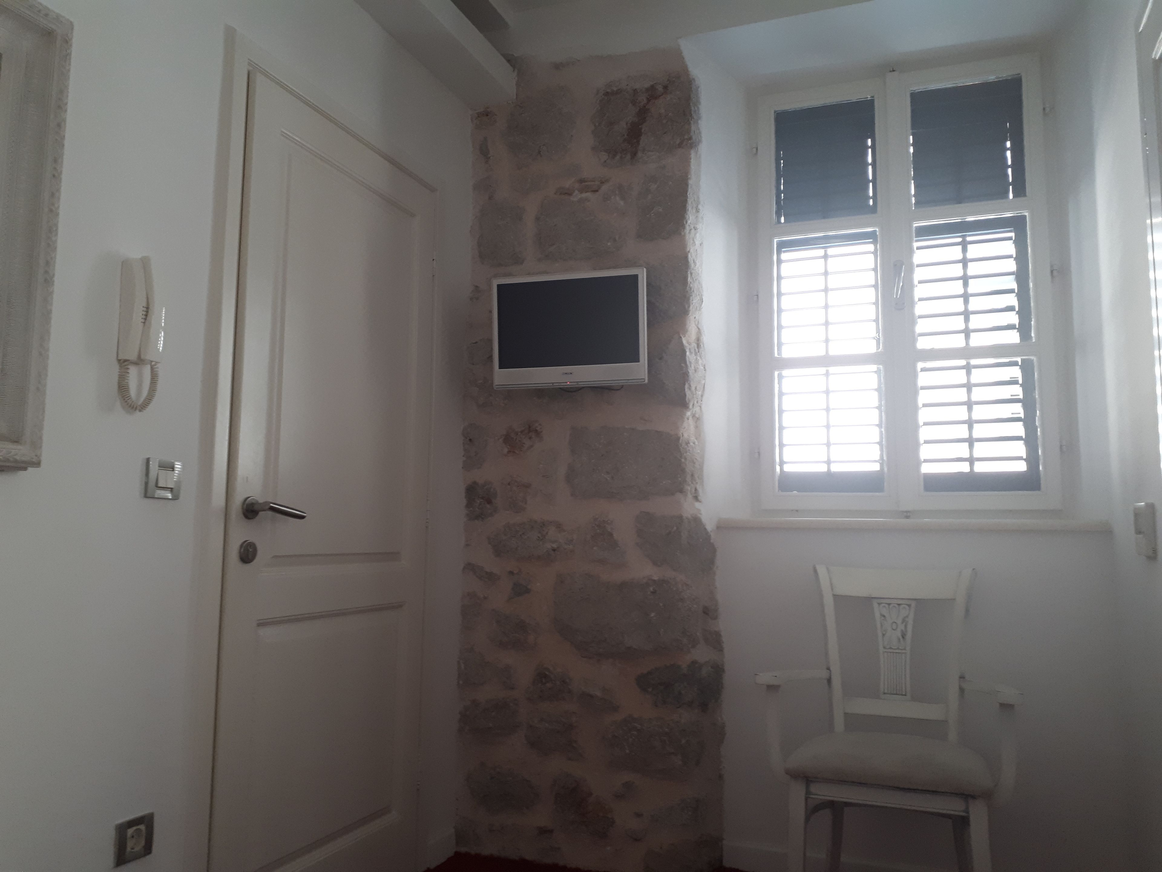 A room with a stone wall, a door, a mounted TV, and a window with blinds.