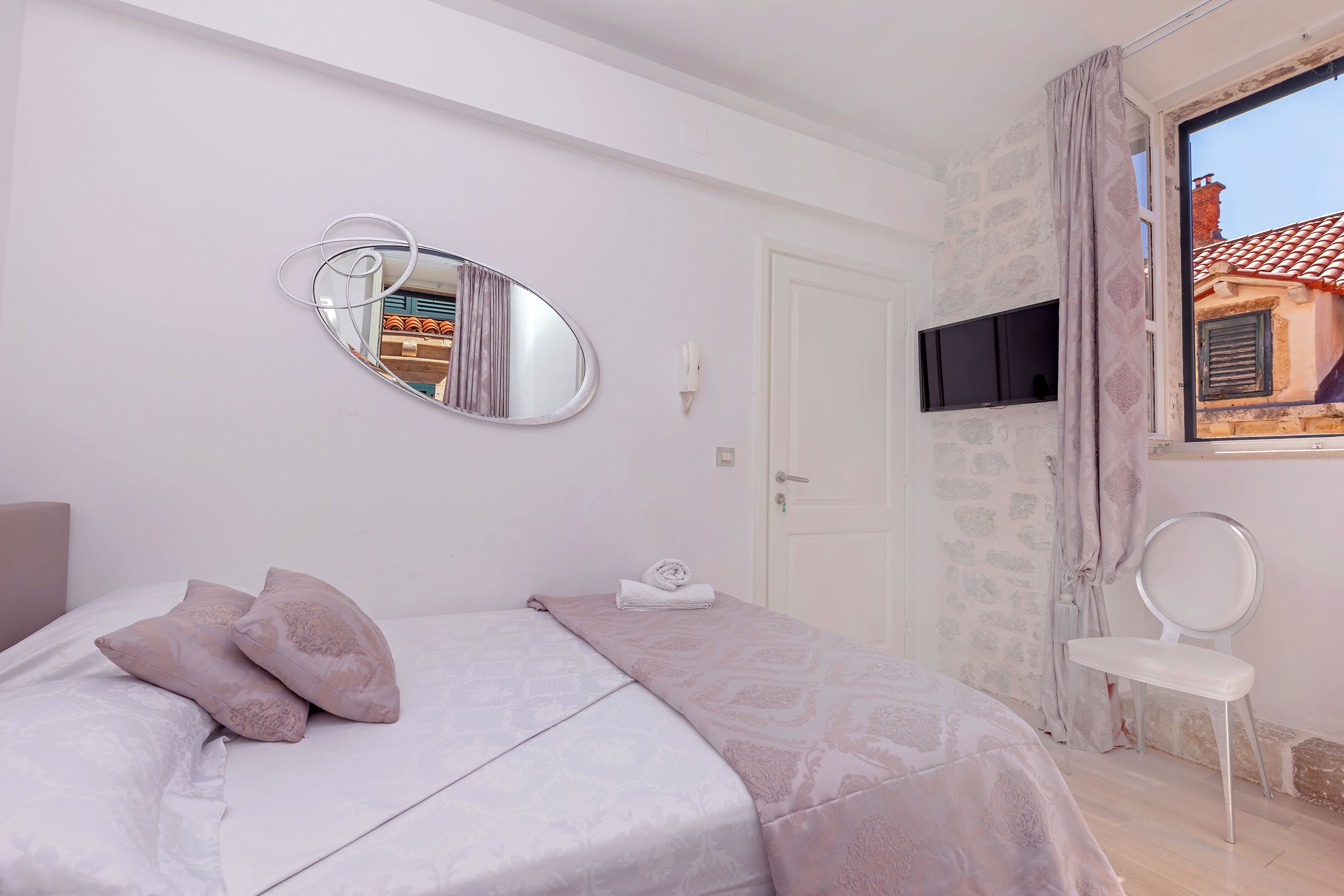 Quarto com uma cama, um espelho, uma televisão e uma janela com cortinas.
