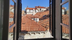 Visão através de uma janela aberta mostrando telhados de terracota e edifícios com paredes de pedra e antenas parabólicas.