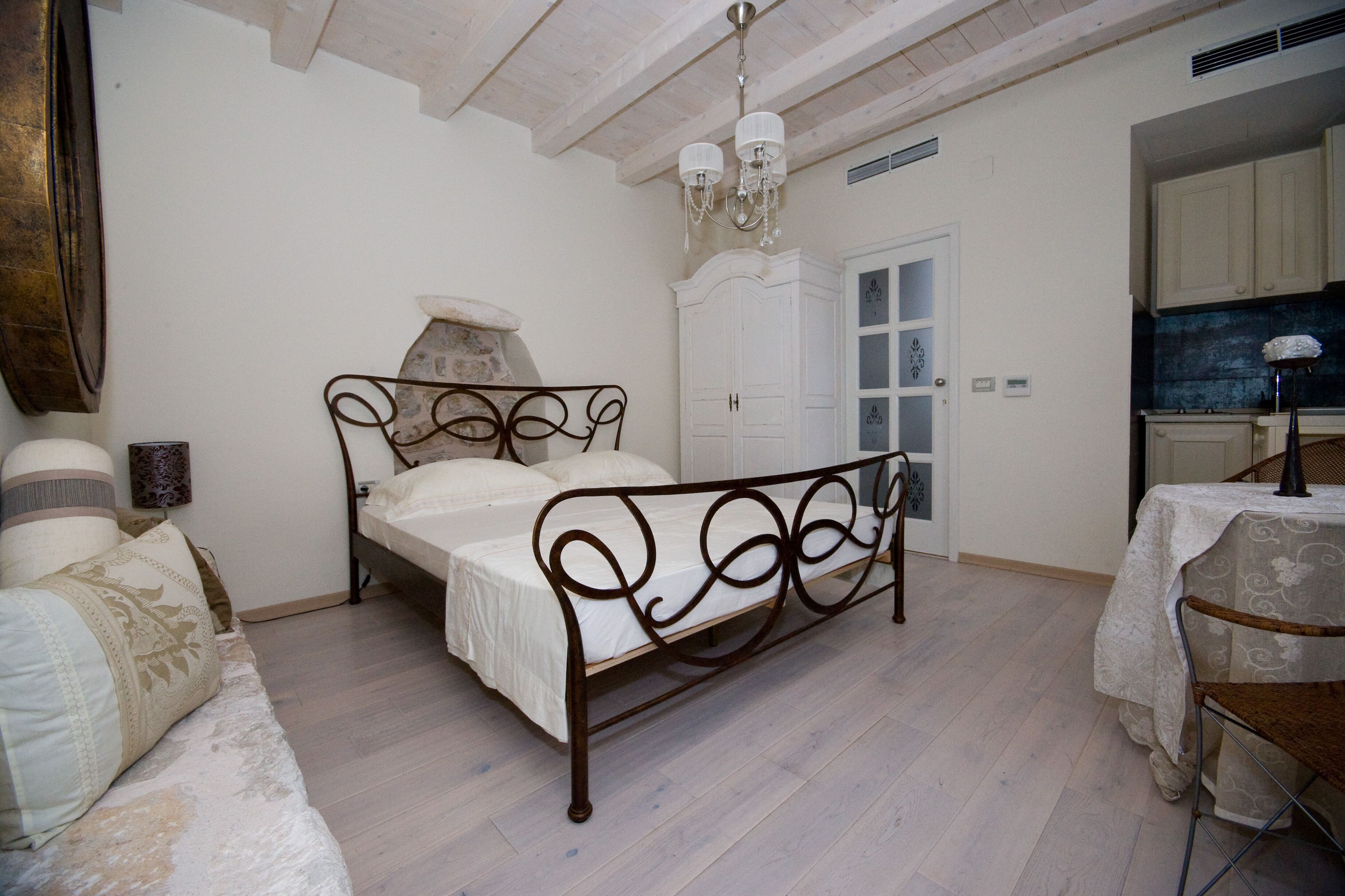 Um quarto com uma cama, um guarda-roupa branco, uma mesa de jantar com cadeiras e um candelabro.