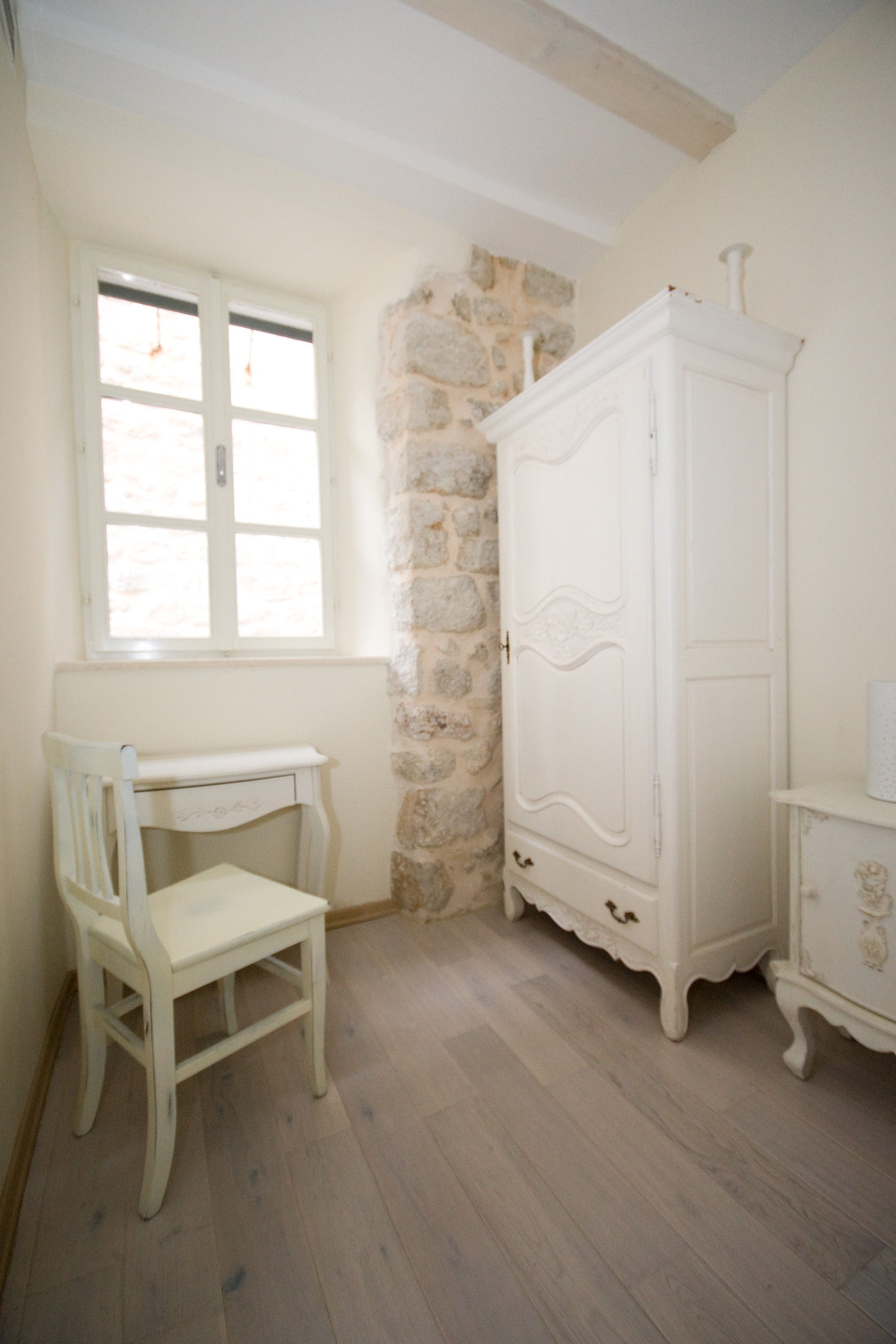 A room with a white chair, a white wardrobe, and a stone wall.