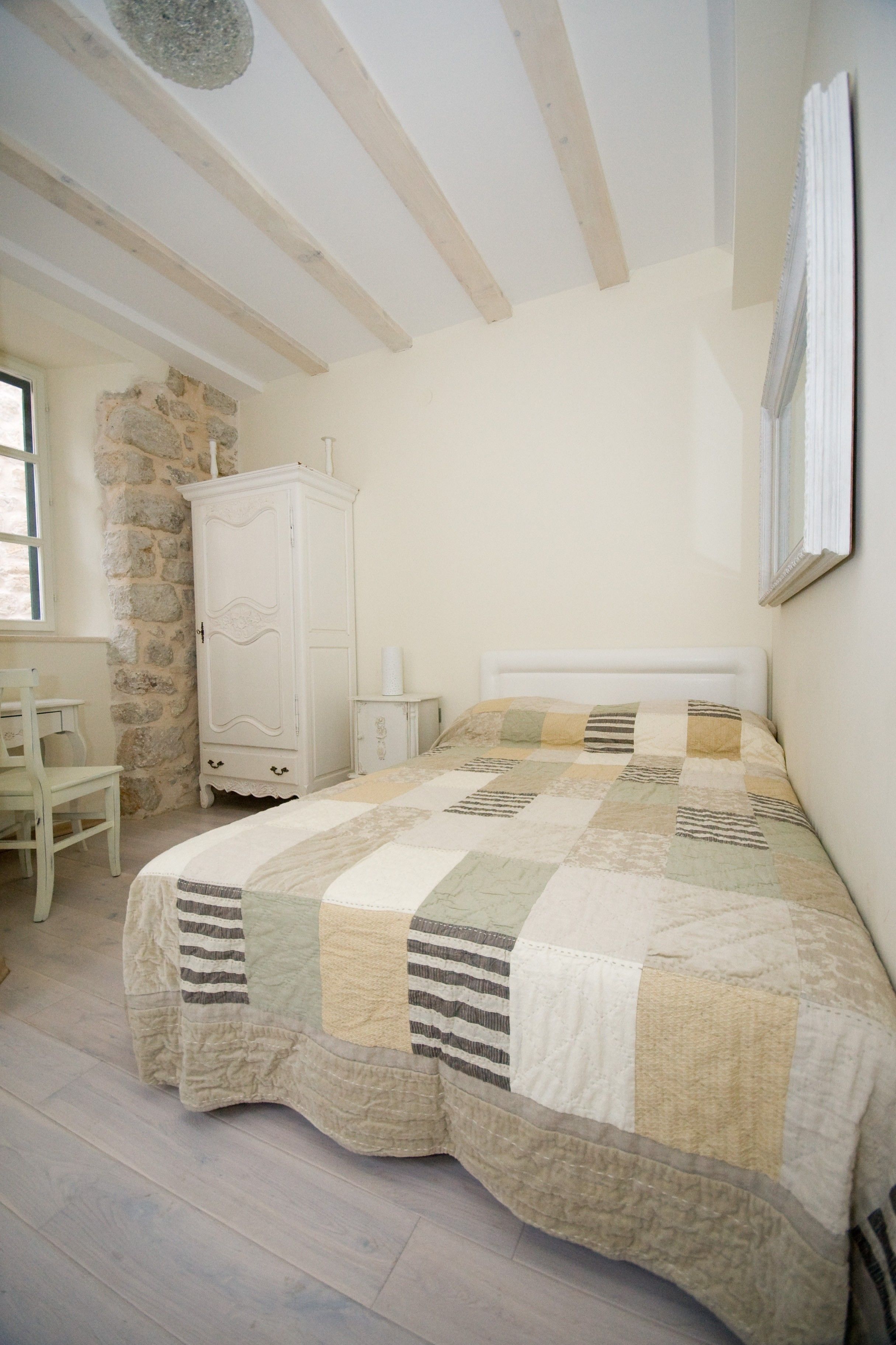 A bedroom with a bed, a white wardrobe, a stone wall, and a window.