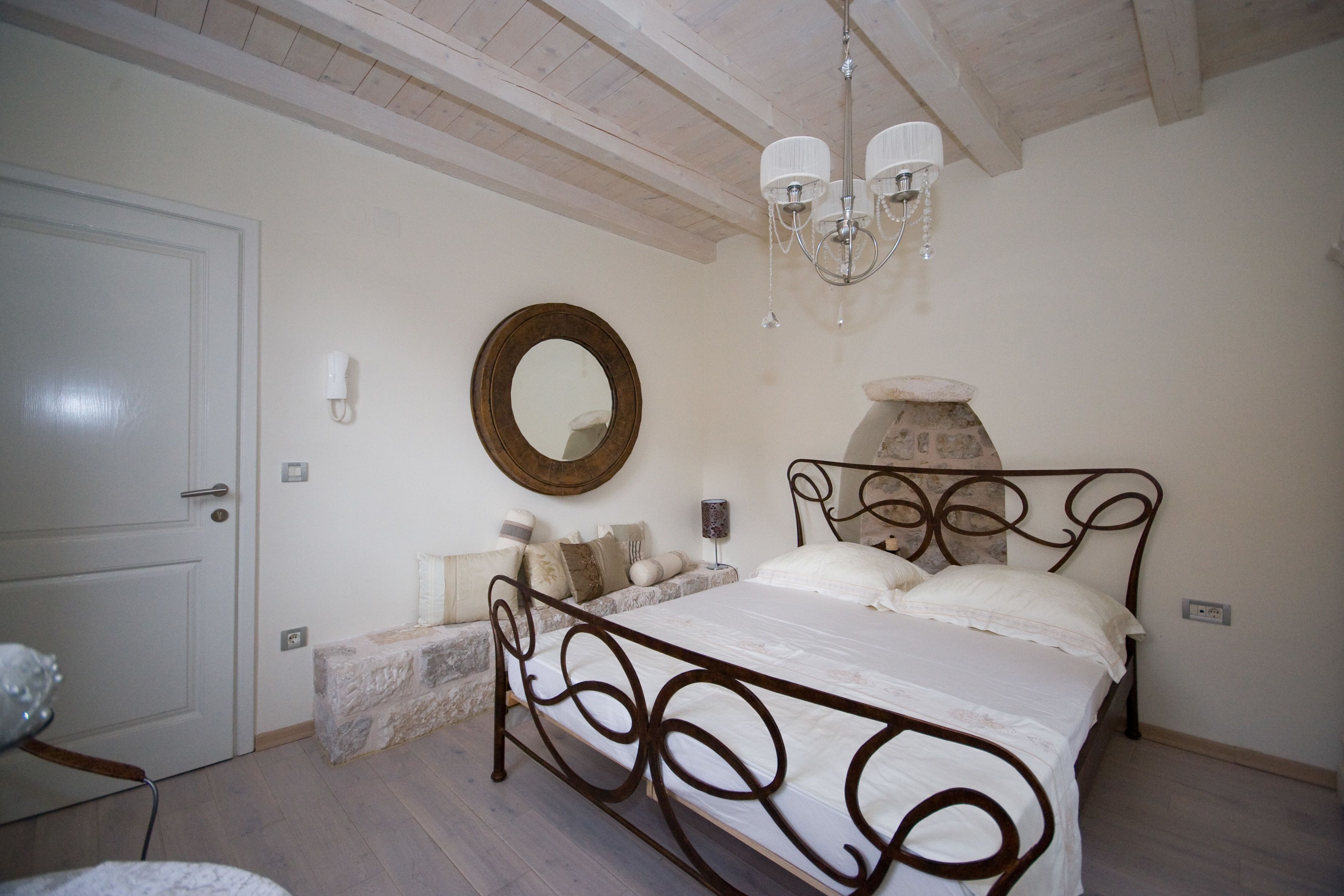 A bedroom with a bed, a round mirror, a chandelier, and a stone fireplace.