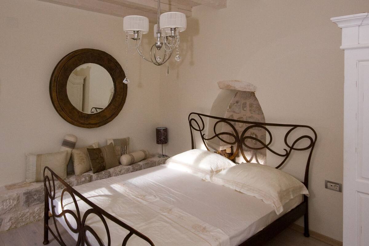 A bedroom with a bed, a chandelier, a round mirror, and a dresser.