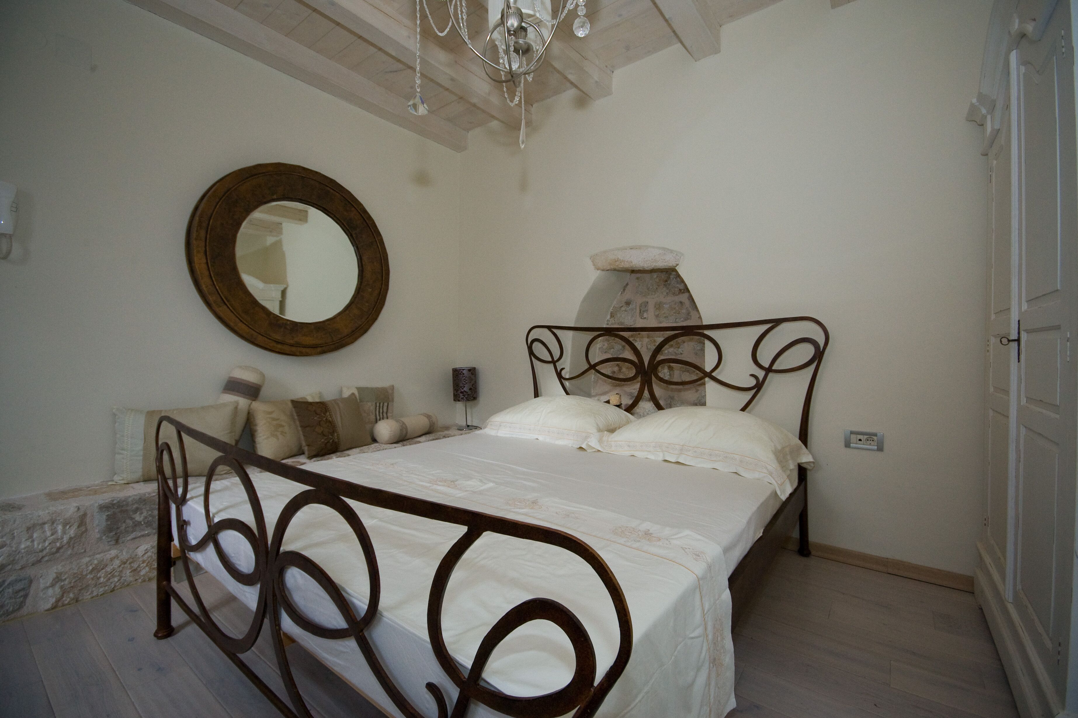 A bedroom with a bed, a round mirror, and a chandelier.