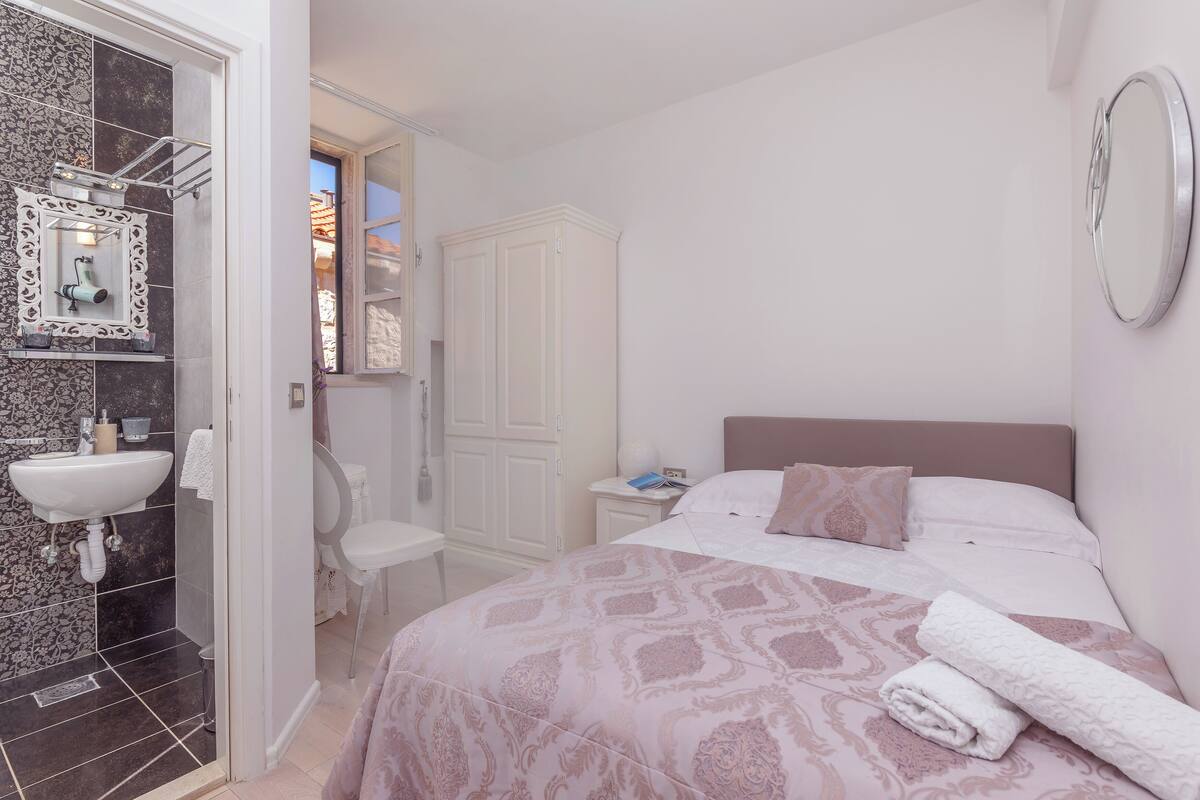 A bedroom with a bed, a bedside table, a mirror, and a bathroom with a sink and toilet.