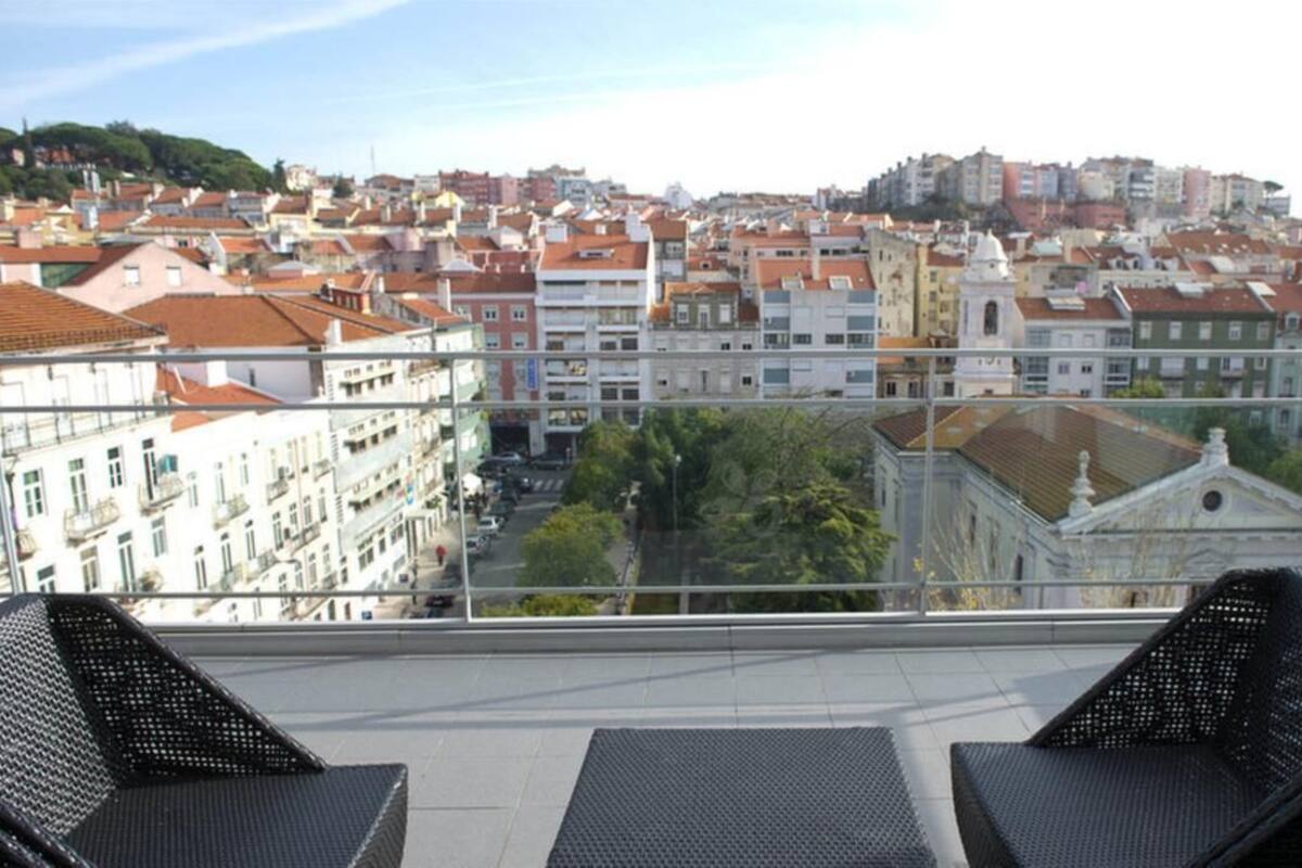 Un balcón con sillas de mimbre que da a una vista panorámica de una ciudad con edificios históricos y una iglesia.