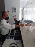 Ένας άνδρας με λευκό πουκάμισο εργάζεται σε ένα γραφείο, μπροστά σε έναν υπολογιστή, με έναν πυροσβεστήρα δίπλα του και διάφορες πινακίδες κρεμασμένες στον τοίχο.