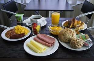 A breakfast table with plates of food, a glass of orange juice, a cup of coffee, and a container of yogurt.
