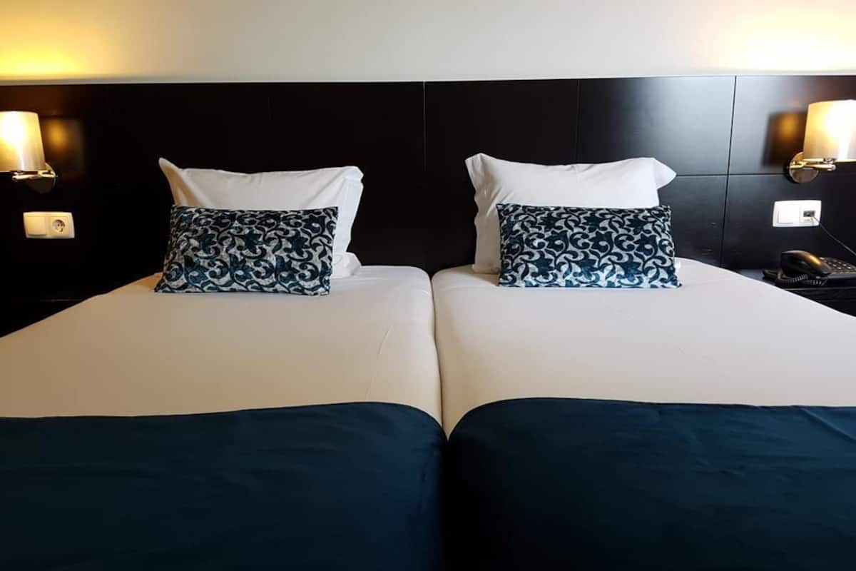 Cama doble con dos almohadas, mesita de noche con lámpara y teléfono.