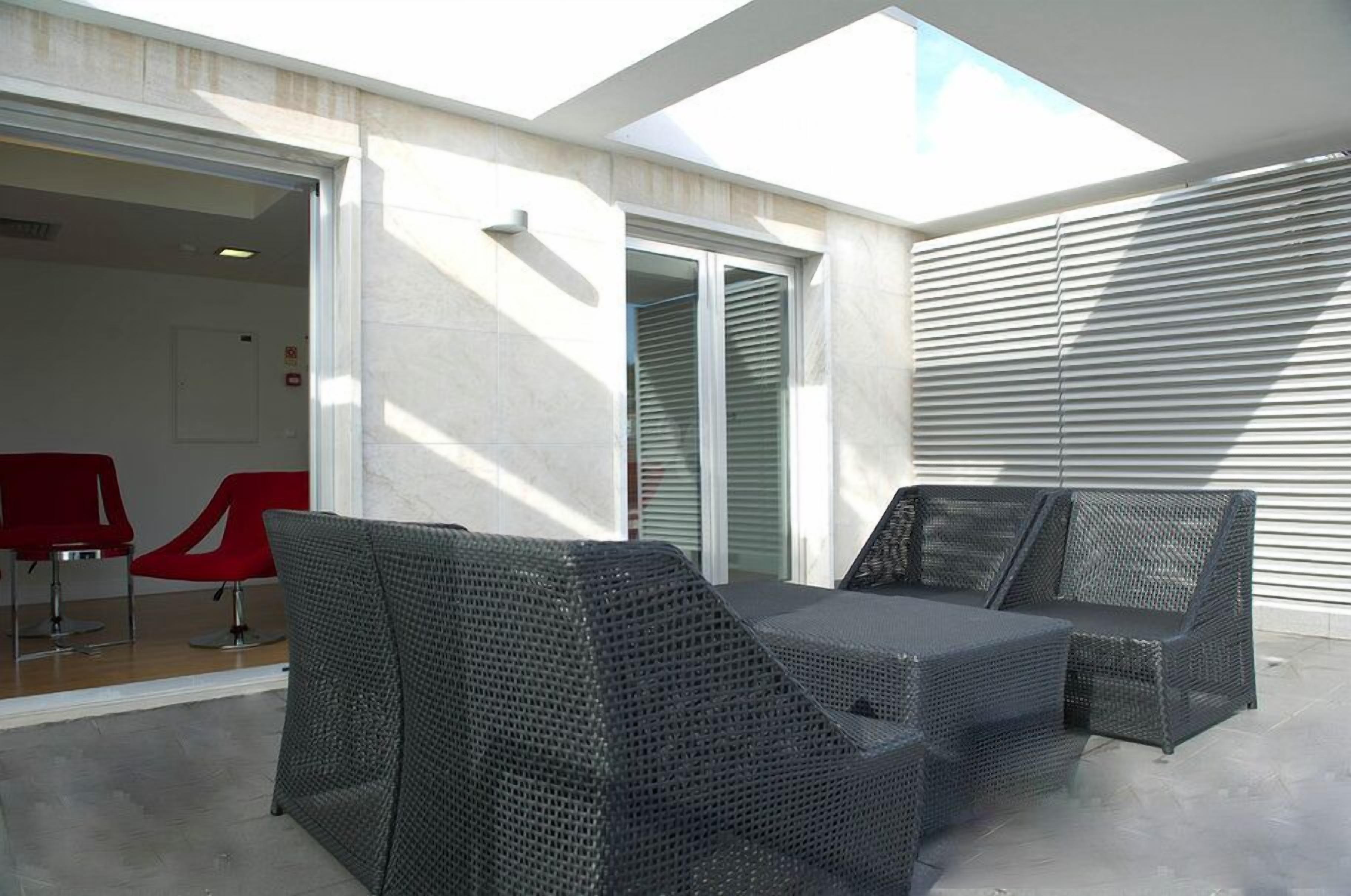Un patio exterior con mobiliario de mimbre, una puerta de cristal que da al interior y vistas al cielo.