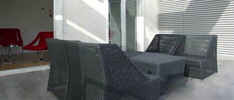 Un patio exterior con mobiliario de mimbre, una puerta de cristal que da al interior y vistas al cielo.