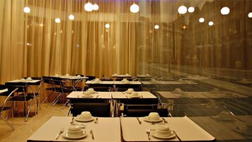 A restaurant with tables set for dining, featuring a view through a large window.