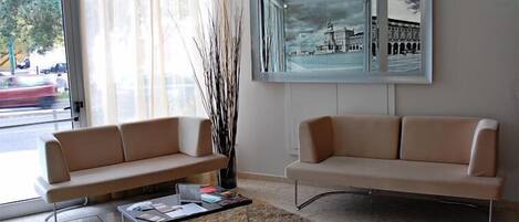 A modern living room with two beige sofas, a glass coffee table, and a large framed cityscape artwork on the wall.