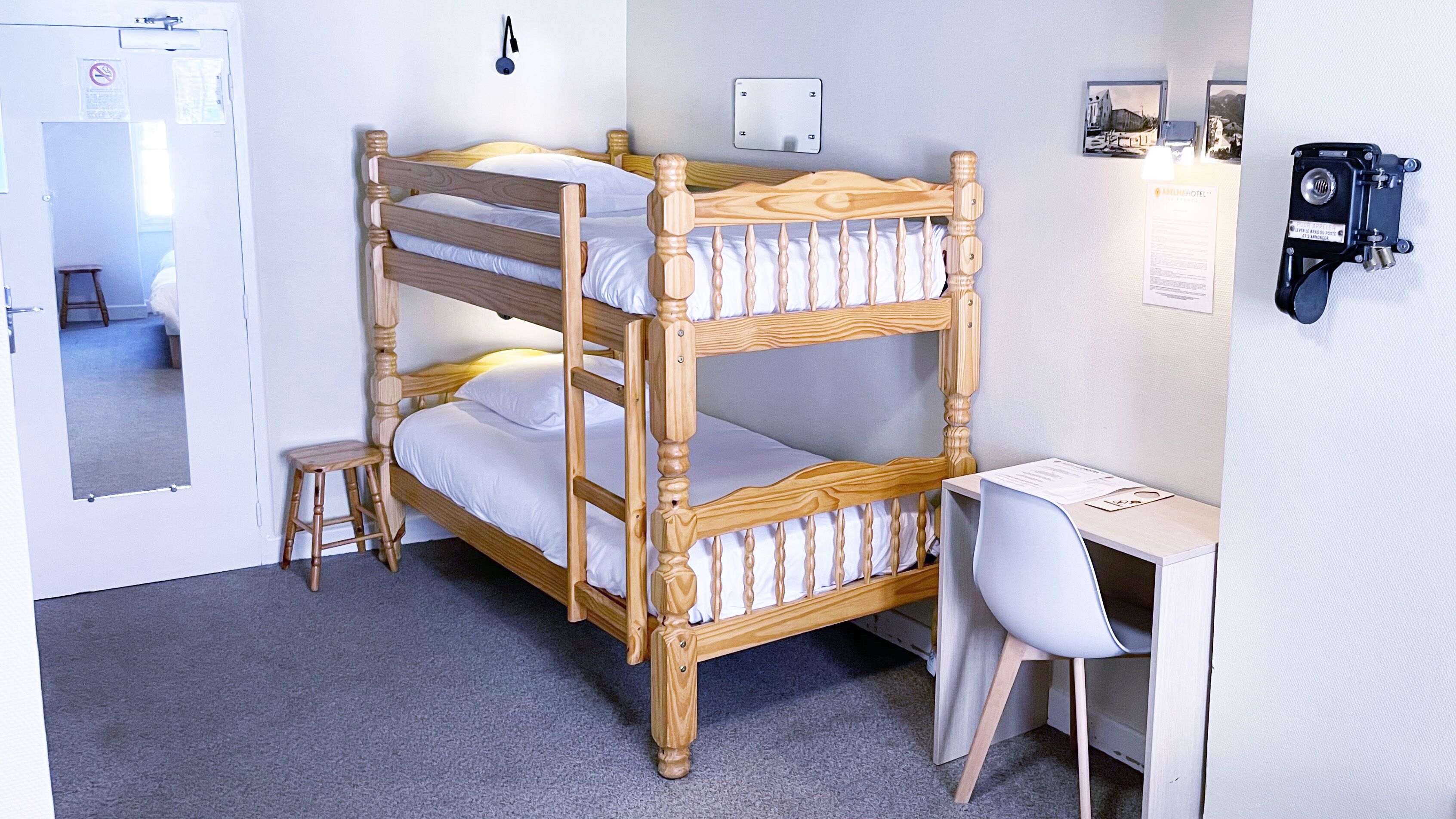 A bunk bed with a desk and chair, a mirror, and a door with a sign.