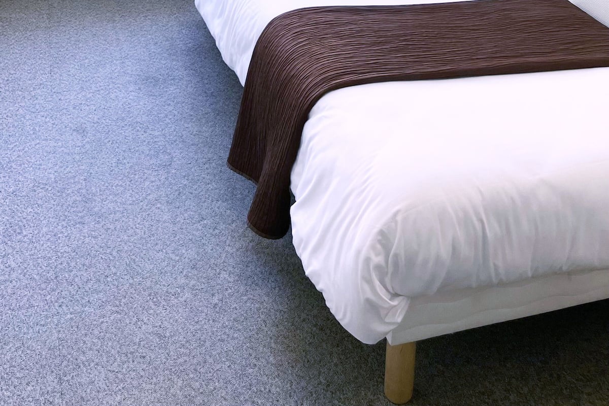 A single bed with a brown blanket, a white pillow, and a window with a view of buildings outside.