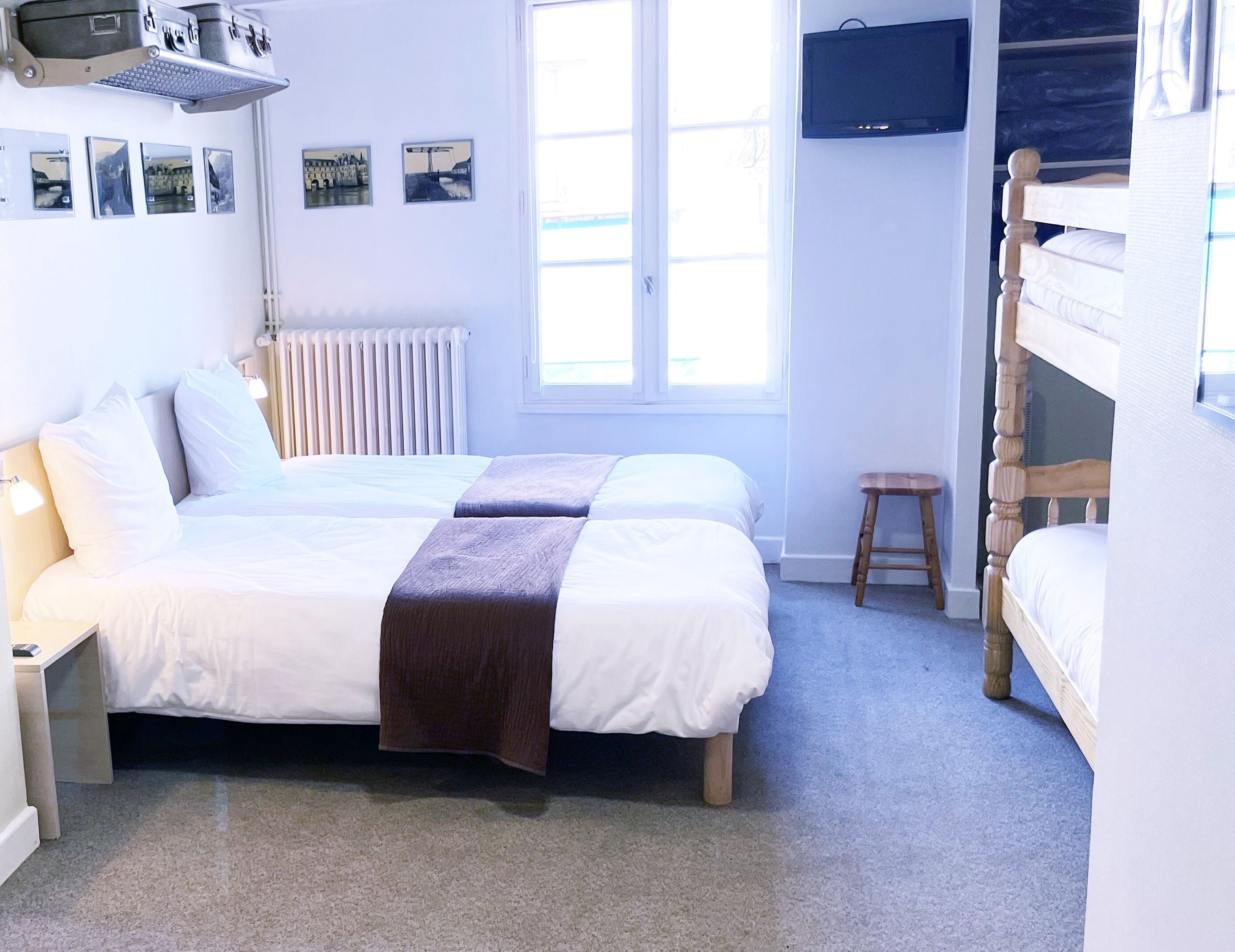 A bedroom with two beds, a small stool, a radiator, and a TV on the wall.