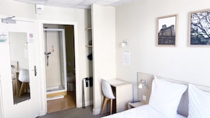 Ein Hotelzimmer mit einem Bett, einem Schreibtisch mit Stuhl, einem kleinen Tisch, einem Nachttisch, einer Wandlampe und einem Bilderrahmen.