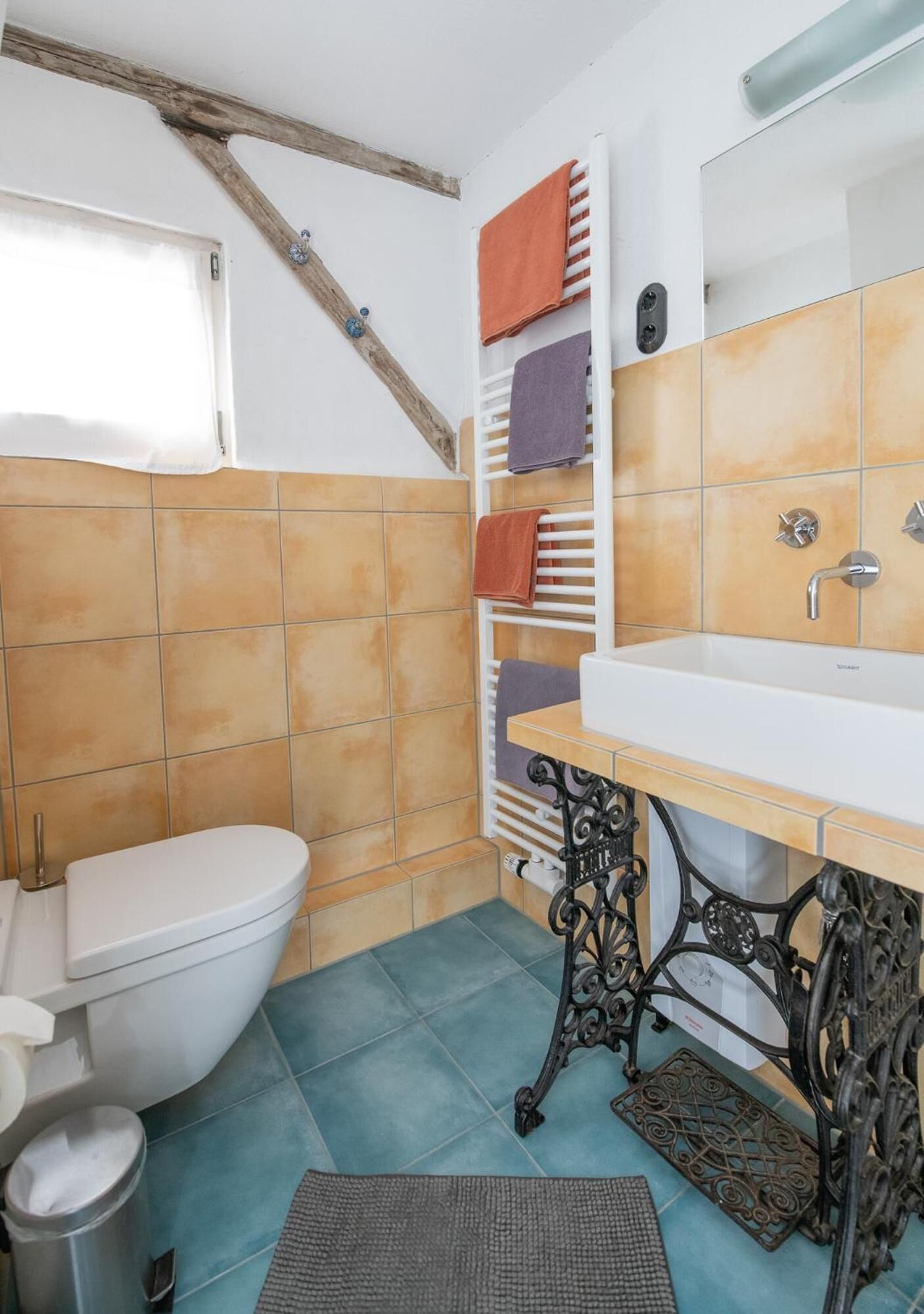 Une salle de bain avec des toilettes blanches, un lavabo avec un miroir et un porte-serviettes avec plusieurs serviettes.
