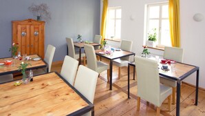 Un comedor con mesas y sillas de madera, un armario de madera y cortinas amarillas en las ventanas.
