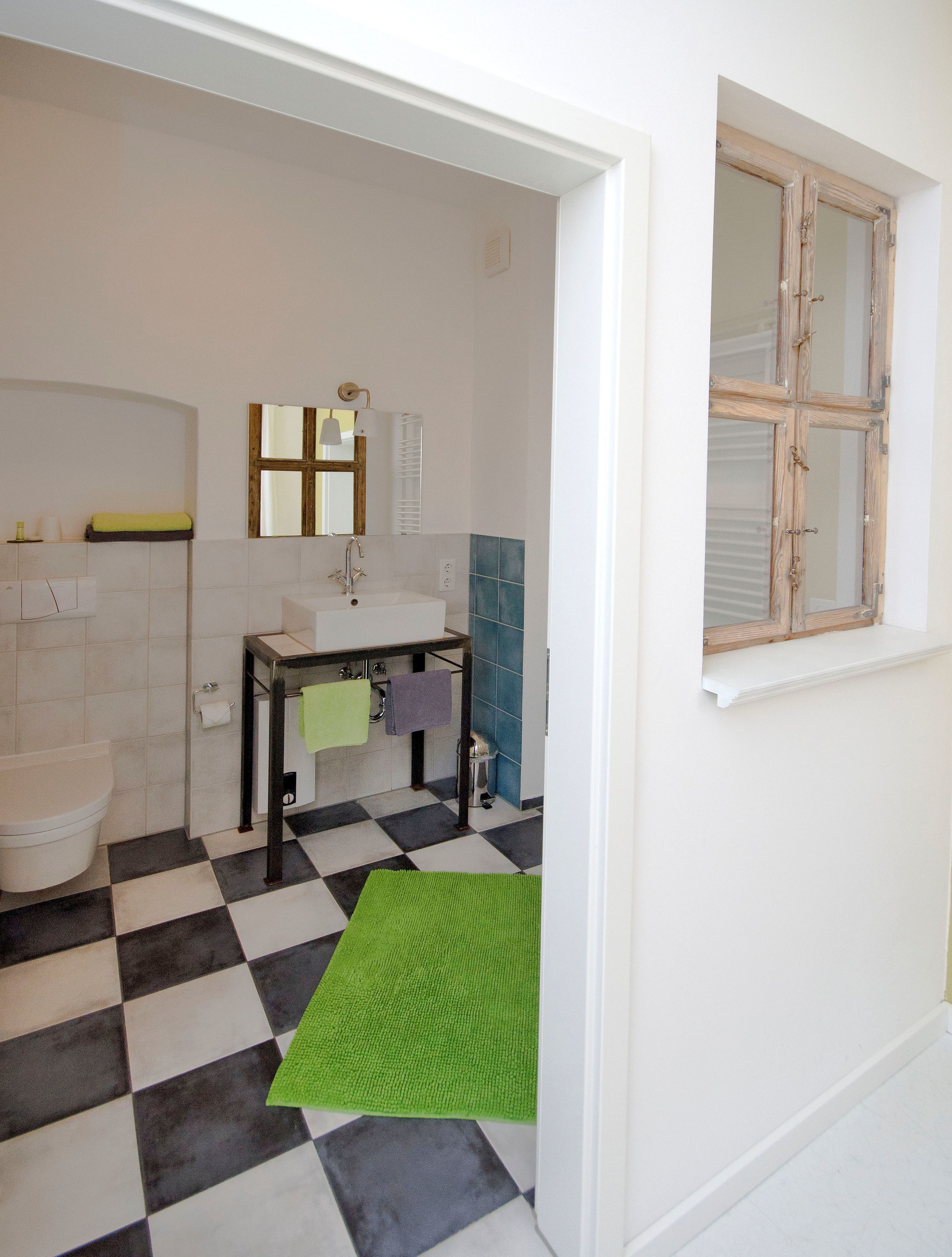 A bathroom with a checkered floor, a sink, a toilet, and a window with wooden frames.