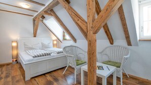 Un dormitorio con techo de madera, una cama, dos sillas de mimbre, una mesita y una ventana.