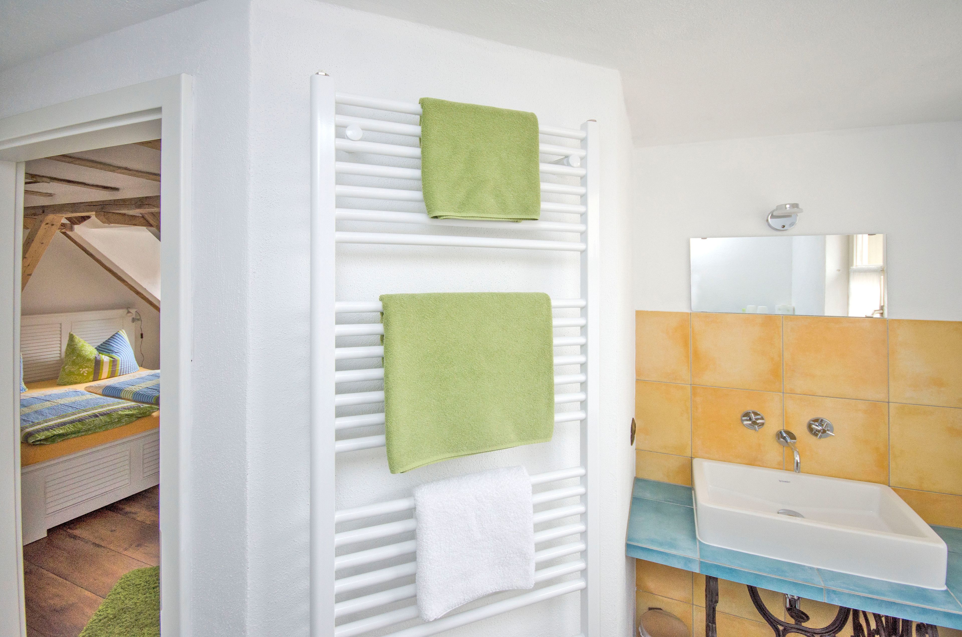 A bathroom with a white sink, a mirror, and a towel rack with two green towels.