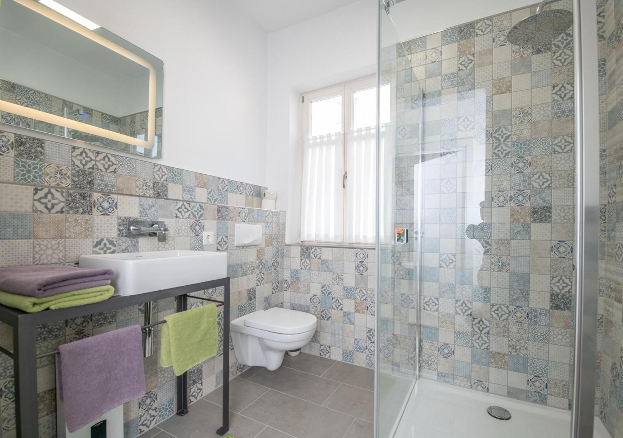 Een badkamer met een betegelde douche, wastafel en toilet.