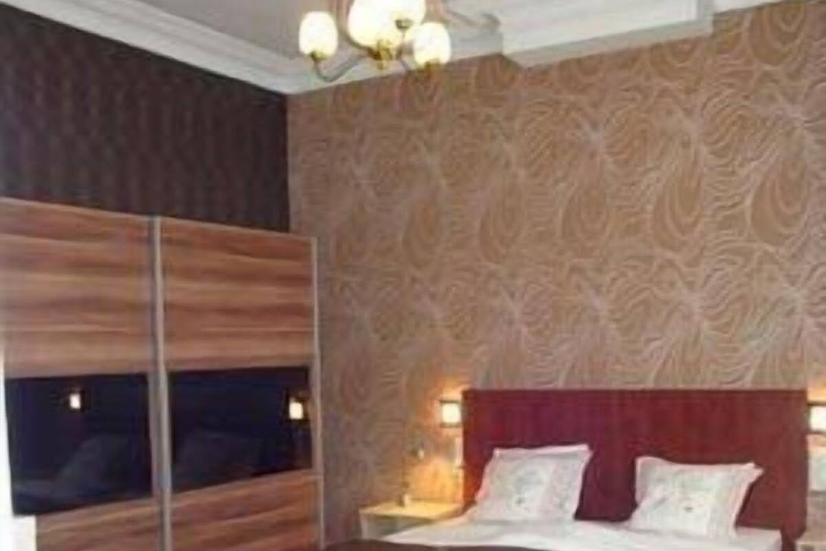 Una habitación de hotel moderna con una cama grande, un armario de madera, un sillón rojo y un papel pintado estampado.