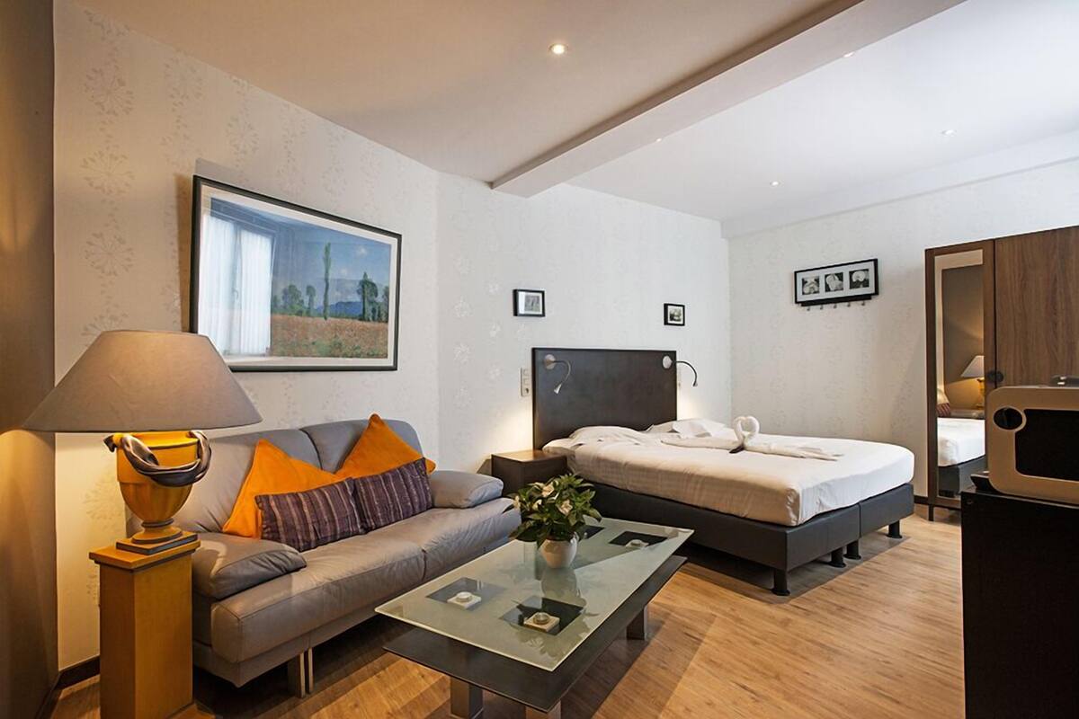 Una habitación de hotel moderna con sofá, cama, mesa de centro de vidrio y lámpara.