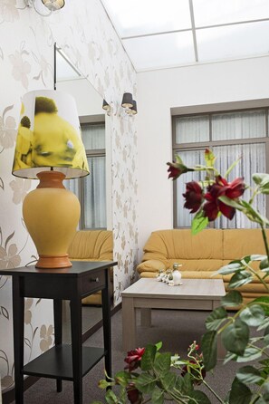 A modern living room with a yellow sofa, a small table with decorative items, and a yellow lamp on a black side table. - Hotel Cathedral Gent Centrum (Ghent)