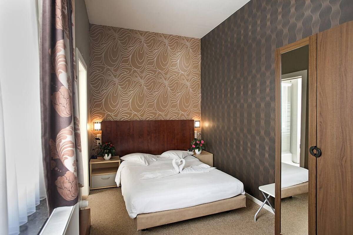 Habitación de hotel con cama, mesitas de noche, un pequeño armario y una mesa.