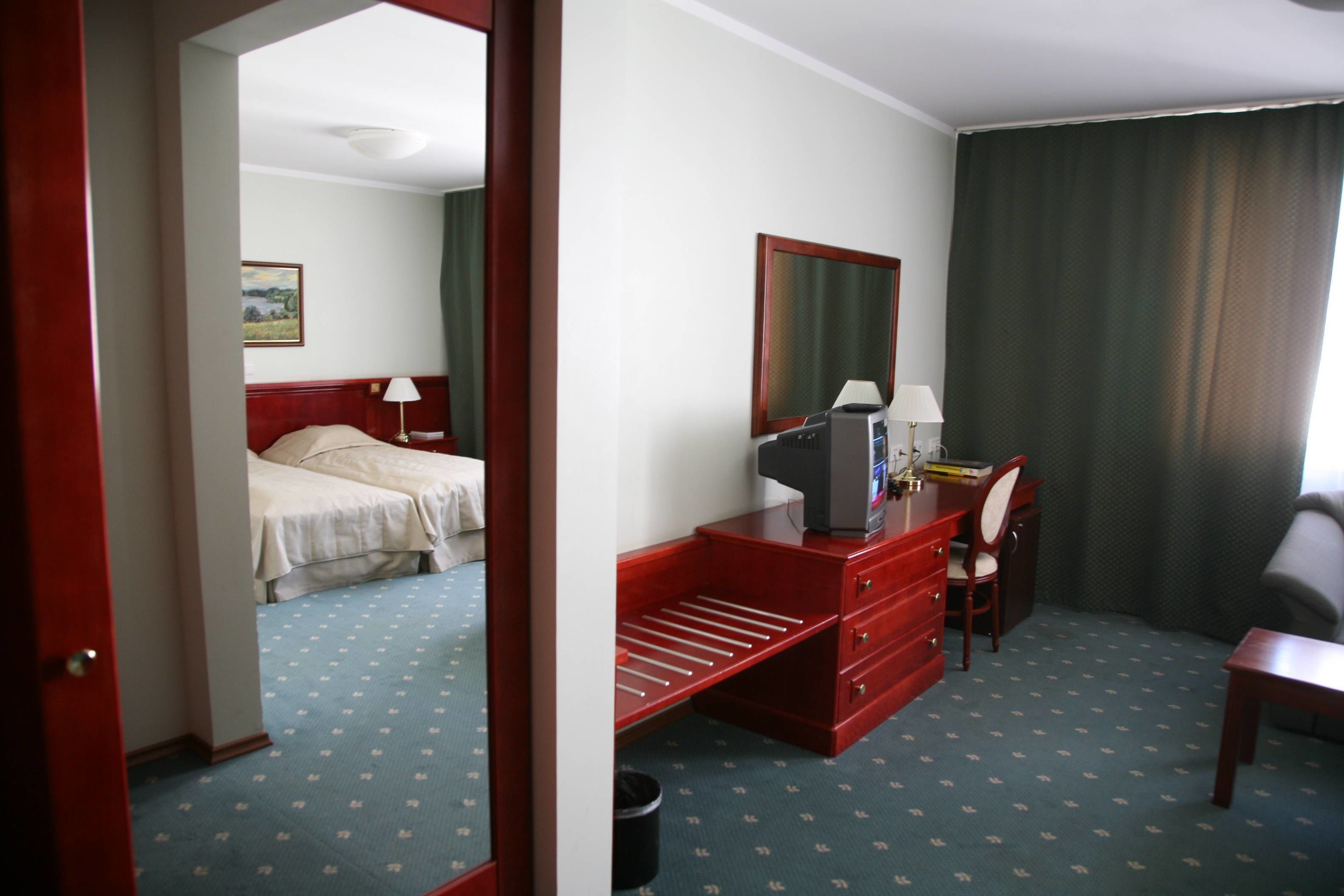 Ein Hotelzimmer mit Bett, Schreibtisch mit Stuhl, Fernseher, Spiegel und einem Fenster mit Vorhängen.