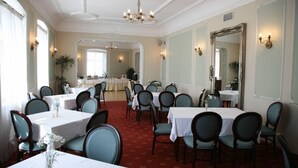 A formal dining room with multiple tables and chairs, a chandelier, and a large mirror on the wall. - Draakon Hotel (Tartu)