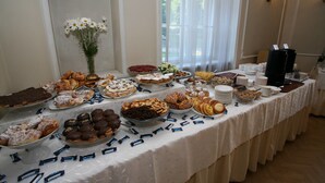 A buffet table with various pastries and desserts, a vase of flowers, and a coffee station. - Draakon Hotel (Tartu)